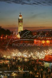 Image du Maroc Professionnelle de  Au coucher du soleil et même un peu avant la foule envahi la fameuse Place Jemaa El Fana qui se métamorphose en un gigantesque restaurant en plein air grâce aux nombreux stands et gargotes qui s'y installent sur ce lieu mythique au centre de la médina de Marrakech. Au fond le minaret de la Koutoubia, Samedi 26 Février 2005. (Photo / Abdeljalil Bounhar)

